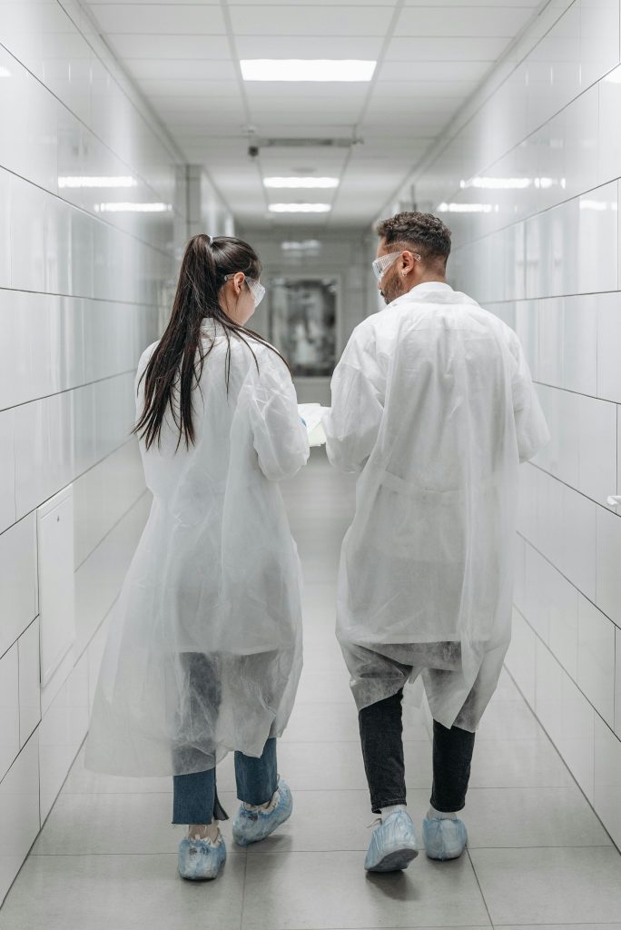 pexels-photo-8442573-8442573 Researchers in lab coats and goggles walking through a laboratory hallway, engaging in teamwork.